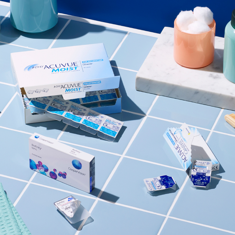 Various contact lens brands in different packaging on a blue tiled background