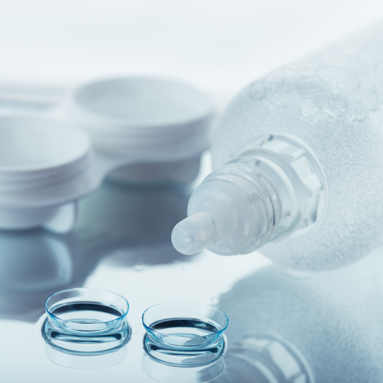 A bottle of contact solution on its side near two contact lenses.