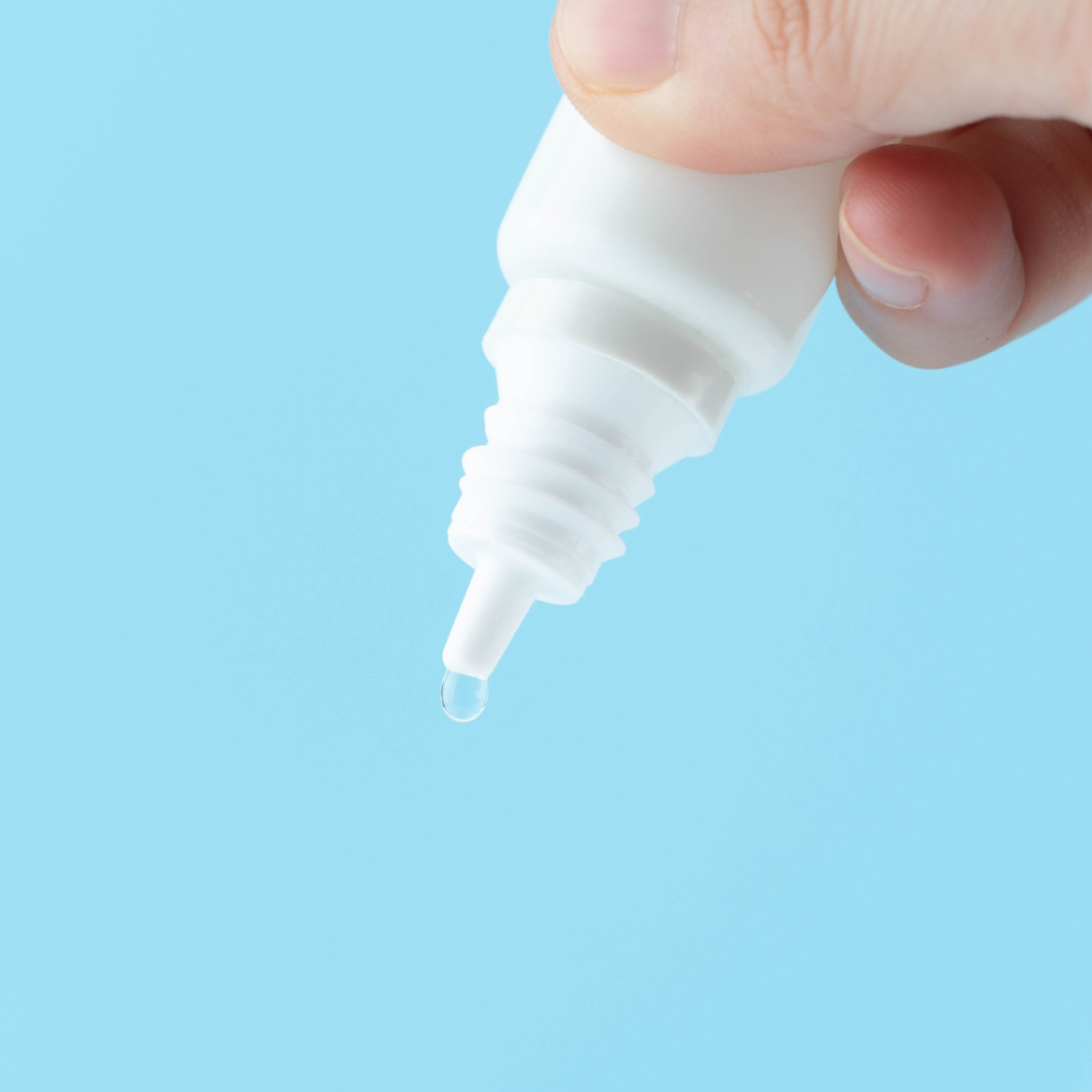 A person squeezing a bottle of eye drops